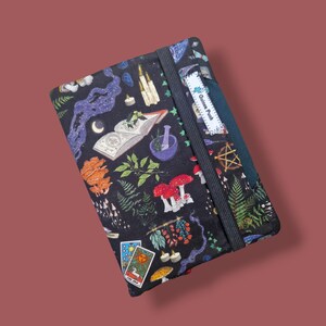 Può includere: Un diario nero con un motivo colorato con funghi, erbe, carte dei tarocchi ed elementi celesti. Il diario ha una chiusura con elastico e un'etichetta con la scritta "Guinea Punk".