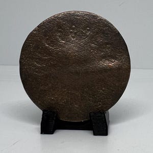 May include: A round, dark brown metal disc on a black stand. The disc has a textured surface.