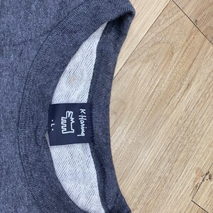 May include: Dark gray crew neck sweatshirt with a white interior. The label reads "K. Haring" with a stylized graphic and the size "-L."
