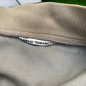 May include: A close-up of a gray cotton shirt with a white label that reads "Kansai Yamamoto".
