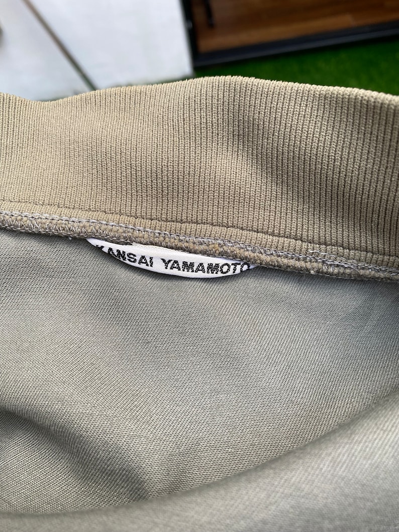 May include: A close-up of a gray cotton shirt with a white label that reads "Kansai Yamamoto".