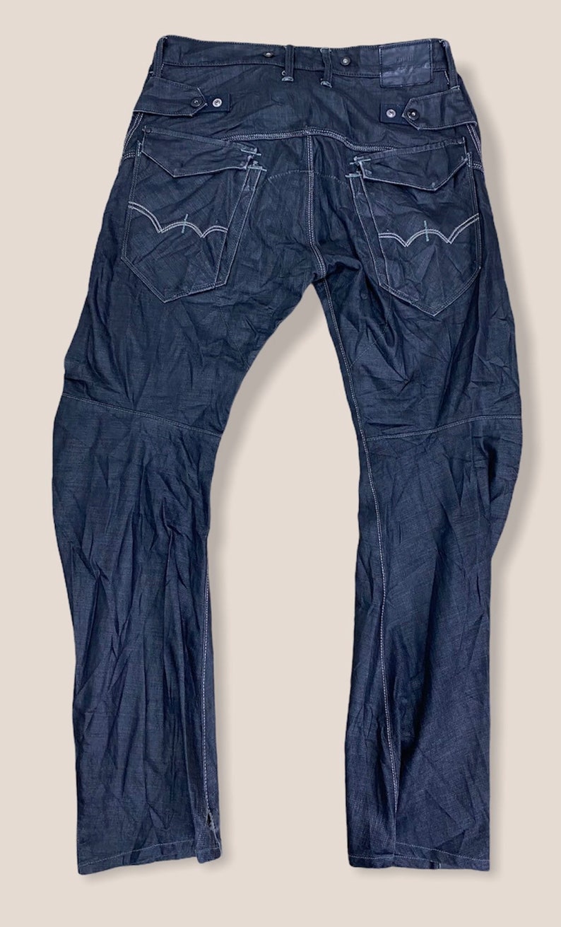 Peut inclure: Un jean en denim bleu fonc&eacute; avec plusieurs poches et des d&eacute;tails de couture. Le jean a une coupe d&eacute;contract&eacute;e et une jambe droite.