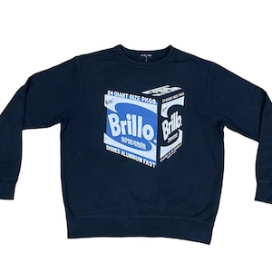 Puede incluir: Una sudadera negra con un gr&aacute;fico blanco de una caja de jab&oacute;n para fregar Brillo. La caja tiene el texto "24 Giant Size Pkgs. New! Brillo Soap Pads. Shines Aluminum Fast." impreso en ella.