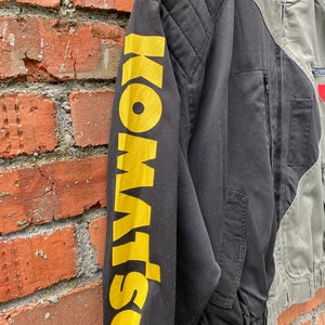 May include: Black and green bomber jacket with a yellow "DSQUARED2" logo on the left sleeve. The jacket has a zipper closure and a ribbed collar.