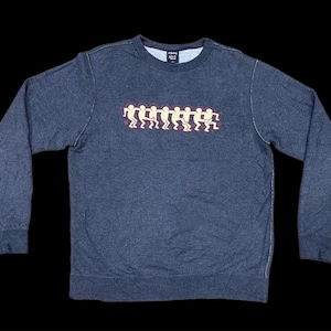 May include: A dark gray sweatshirt with a crew neck and long sleeves. The front features a graphic of stylized figures in a line, in white and red. The sweatshirt is made of a soft, comfortable material.