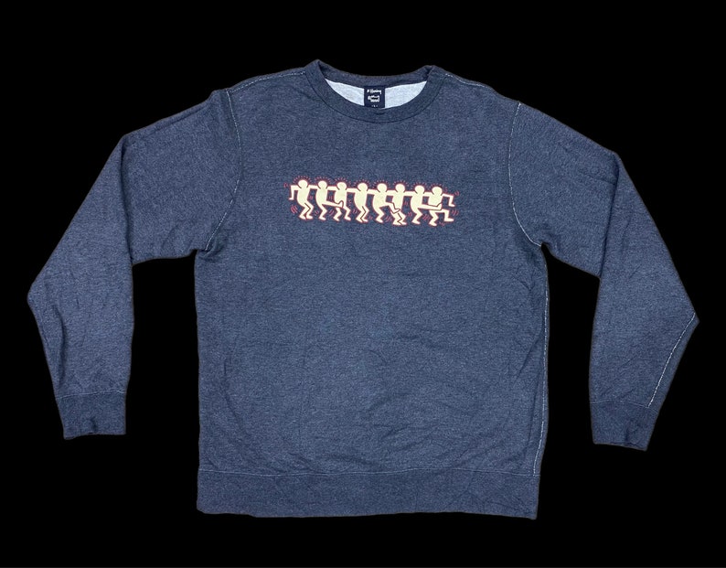 May include: A dark gray sweatshirt with a crew neck and long sleeves. The front features a graphic of stylized figures in a line, in white and red. The sweatshirt is made of a soft, comfortable material.