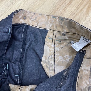 Peut inclure: Gros plan de l'int&eacute;rieur d'un jean bleu fonc&eacute; avec une doublure &agrave; motif camouflage. Le jean porte une &eacute;tiquette "EDWIN" et "1001".
