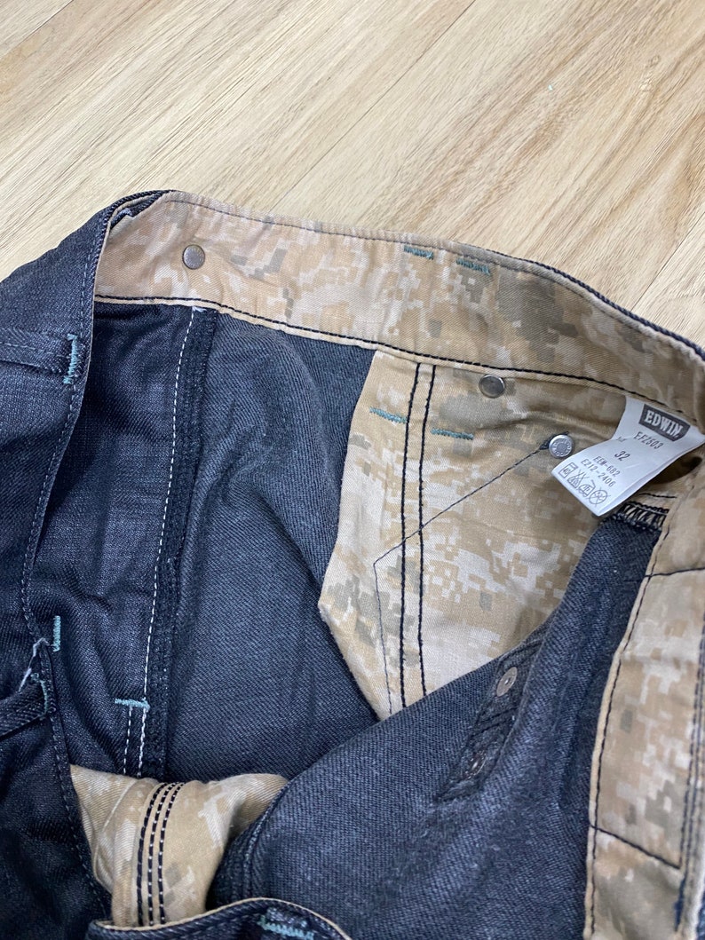 Peut inclure: Gros plan de l'int&eacute;rieur d'un jean bleu fonc&eacute; avec une doublure &agrave; motif camouflage. Le jean porte une &eacute;tiquette "EDWIN" et "1001".