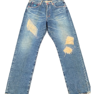 May include: A pair of blue denim jeans with distressed patches on the knees and thighs. The jeans have a straight leg fit and a classic five-pocket style.