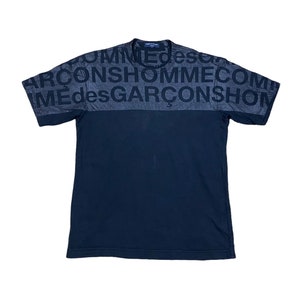 May include: Black short-sleeved t-shirt with a black and gray print on the front. The print says "COMME des GARCONS HOMME" repeated.
