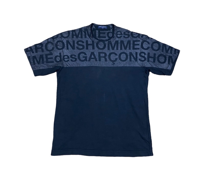 May include: Black short-sleeved t-shirt with a black and gray print on the front. The print says "COMME des GARCONS HOMME" repeated.