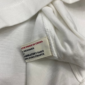 May include: White clothing tag with red text that reads "With pride in China" and "Designed by Laboratory Paris 1001 Paris, France".