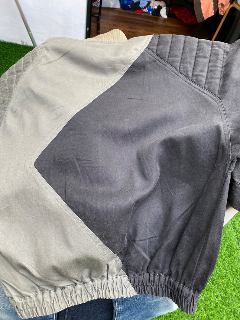May include: A black and gray bomber jacket with a quilted design on the sleeves and a contrasting gray panel on the back.