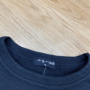 Puede incluir: Sudadera negra con una etiqueta negra que dice "And Wander" y "M" para el tama&ntilde;o.