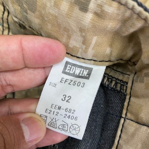 Peut inclure: Un tissu camouflage brun et beige avec une &eacute;tiquette noire qui indique "EDWIN" et "EFZ503". L'&eacute;tiquette indique &eacute;galement "Taille 32", "EEM-682" et "E212-2406".