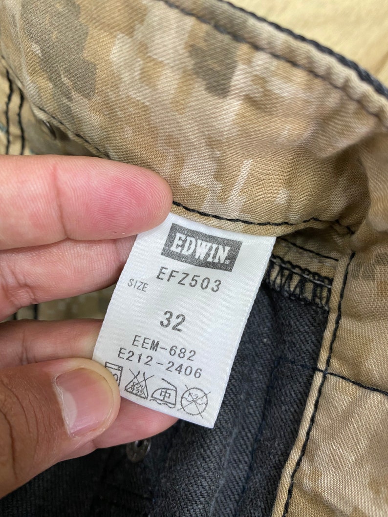 Peut inclure: Un tissu camouflage brun et beige avec une &eacute;tiquette noire qui indique "EDWIN" et "EFZ503". L'&eacute;tiquette indique &eacute;galement "Taille 32", "EEM-682" et "E212-2406".