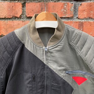 May include: A black and green bomber jacket with a zipper closure and a red triangle patch on the right sleeve.