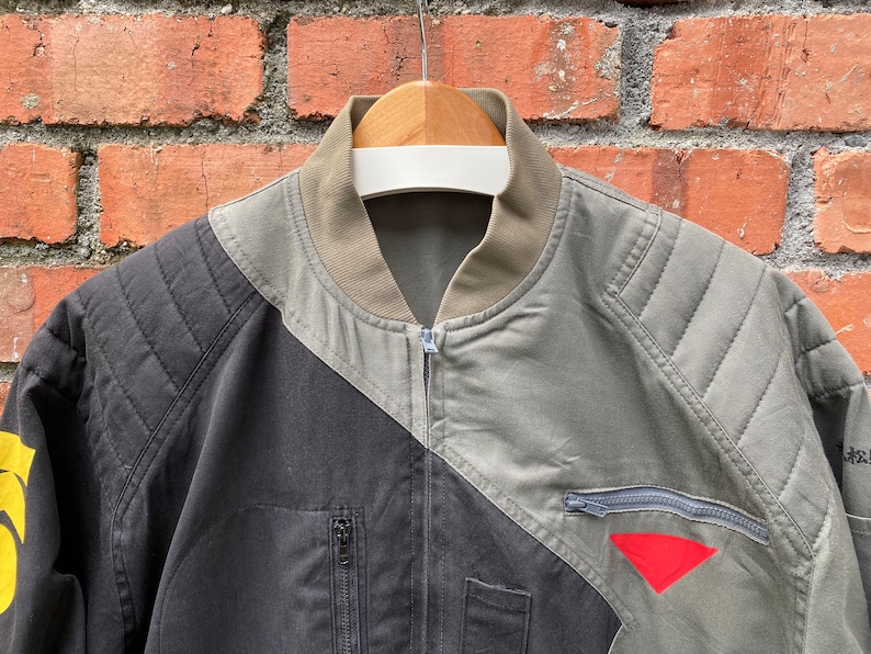 May include: A black and green bomber jacket with a zipper closure and a red triangle patch on the right sleeve.