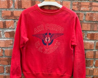 May include: Red sweatshirt with a vintage U.S. Army Air Corps logo featuring a propeller plane with wings. The logo is printed in blue and white.
