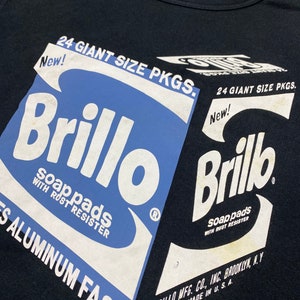 Puede incluir: Camiseta negra con un gr&aacute;fico blanco de una caja de jab&oacute;n Brillo azul y blanco. El texto en la caja dice "24 Giant Size Pkgs. New! Brillo Soap Pads With Rust Resister" y "Brillo Mfg. Co., Inc. Brooklyn, N.Y. Made in U.S.A."
