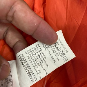 May include: A white tag with black text detailing care instructions and manufacturing information for a garment. The tag includes the text "MADE IN VIETNAM", "WORLVI TRADING", and "080-333-0633".