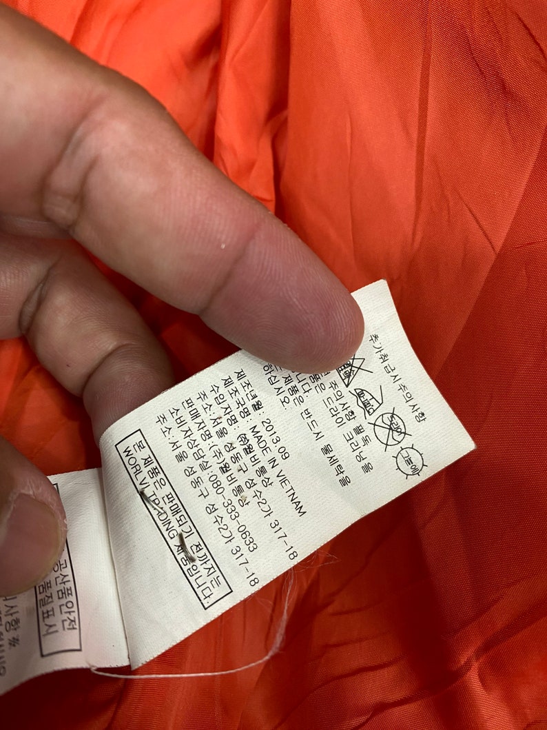 May include: A white tag with black text detailing care instructions and manufacturing information for a garment. The tag includes the text "MADE IN VIETNAM", "WORLVI TRADING", and "080-333-0633".