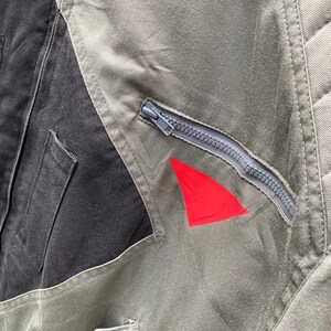 May include: A close-up of a green and black jacket with a zipper and a red triangle patch. The jacket has a quilted design on the back.