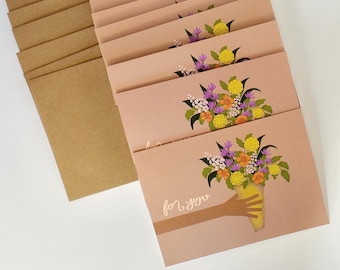 Könnte beinhalten: Blassrosa Grußkarten mit einer floralen Bouquet-Illustration und den Worten "for you". Das Bouquet zeigt gelbe, lila und orangefarbene Blumen, die in einer gelben Vase gehalten werden. Kraftpapierumschläge sind sichtbar.