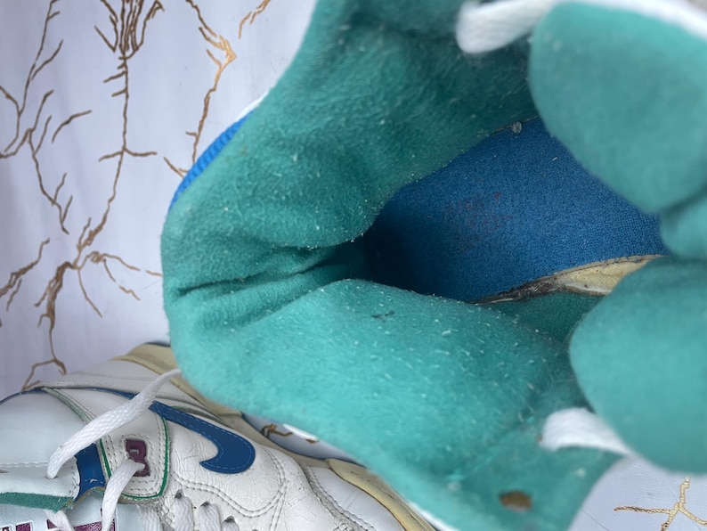 Puede incluir: Primer plano del interior de una zapatilla blanca con forro azul turquesa y leng&uuml;eta blanca. La zapatilla tiene suela blanca y un logotipo Swoosh azul.