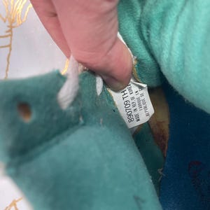 Puede incluir: Primer plano del interior de una zapatilla de deporte azul y turquesa con cordones blancos. La etiqueta dice "890709 TH MADE IN REP. OF KOREA".
