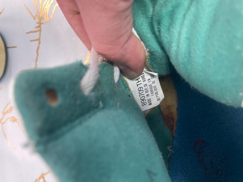 Puede incluir: Primer plano del interior de una zapatilla de deporte azul y turquesa con cordones blancos. La etiqueta dice "890709 TH MADE IN REP. OF KOREA".