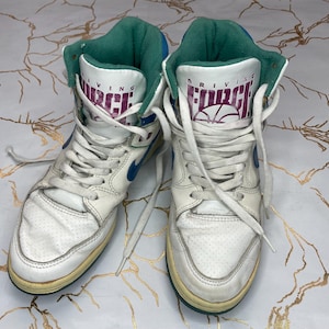 Puede incluir: Un par de zapatillas blancas de ca&ntilde;a alta con detalles en azul y verde. Las zapatillas tienen el texto "Driving Force" en el lateral.