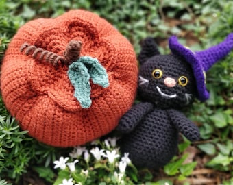 May include: A crocheted orange pumpkin with green leaves and a black crocheted cat wearing a purple witch hat.