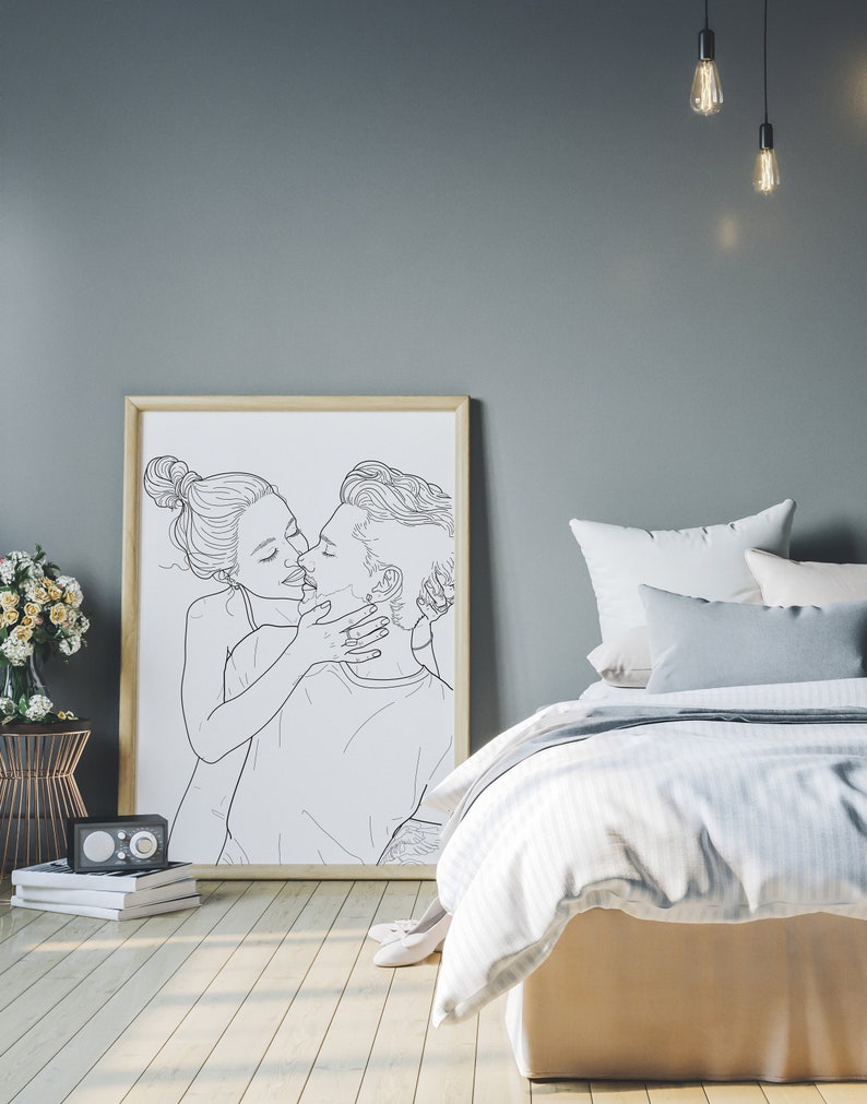 May include: A black and white line drawing of a couple kissing. The drawing is framed and hanging on a wall in a bedroom. The bedroom has a bed with white bedding and a gray headboard.