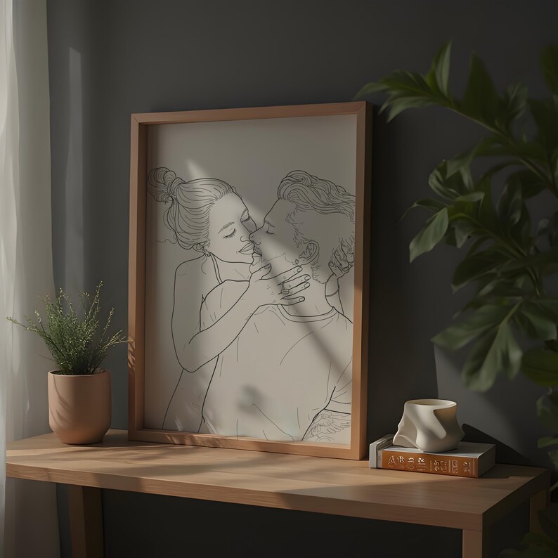 May include: A black and white line drawing of a couple kissing. The drawing is framed in a light wood frame and is hanging on a wall.