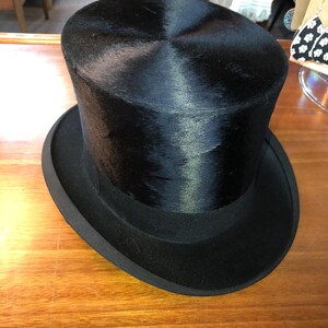 May include: A black top hat with a tall, cylindrical crown and a wide, flat brim. The hat is made of a smooth, shiny material.