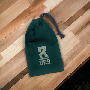 Peut inclure: Une pochette à cordon de serrage vert foncé avec un logo brodé blanc qui dit "R UCS".
