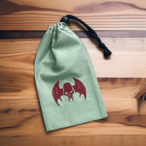 Peut inclure: Un sac à cordon vert avec un crâne rouge brodé avec des ailes. Le sac a un cordon noir.