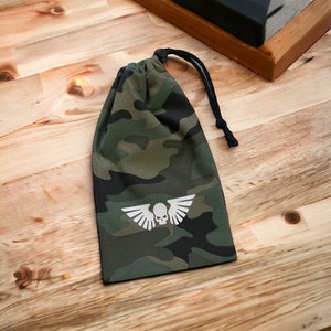 May include: A green and black camouflage drawstring bag with a white skull and wings logo.