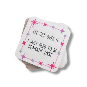 May include: A stack of square white coasters with rounded corners. The top coaster features a pink border with star shapes and the black text: I'LL GET OVER IT I JUST NEED TO BE DRAMATIC FIRST. The design includes small purple and pink stars.