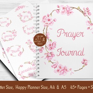 May include: A white prayer journal with a pink floral design on the cover. The cover features a wreath of pink cherry blossoms with the words "Prayer Journal" in pink script. The journal also includes stickers with words like "love", "pray", "joy", "hope", and "trust".