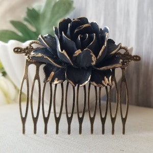 May include: A dark blue and gold floral hair comb. The comb features a large, detailed rose with gold accents, mounted on a bronze-coloured comb base. The comb has multiple tines for securing it in the hair.