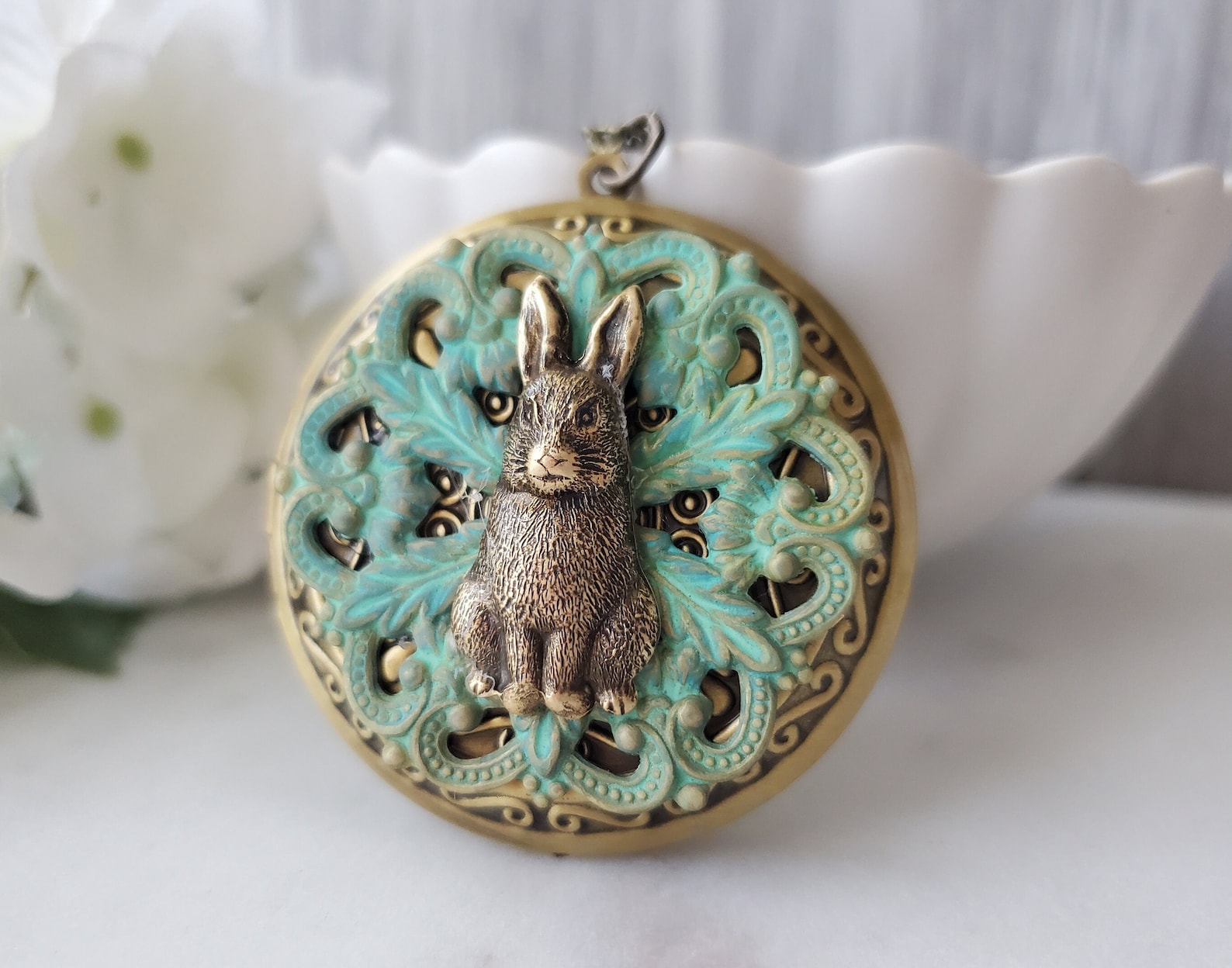 vintage looking locket with a rabbit on the front.  Surrounded by green leaves.