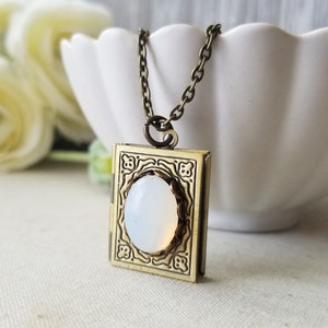 May include: A gold locket necklace with an ornate design and a white opal stone in the center.