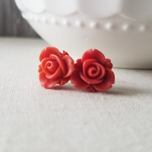 May include: A pair of coral red rose-shaped stud earrings.