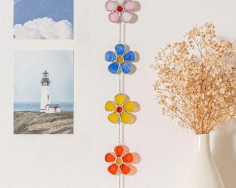 Könnte beinhalten: Eine Girlande aus Buntglasblumen mit vier Blumen in Pink, Blau, Gelb und Orange. Die Blumen sind durch eine silberne Kette verbunden.