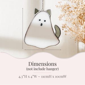 May include: A stained glass cat-shaped suncatcher with a white body, gray ears, and tail. The cat has black eyes and a mouth. The dimensions are 4.3 inches high by 4 inches wide. It hangs from a silver chain.