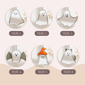 May include: Six different styles of stained glass ghost ornaments, each hanging from a silver chain. The ghosts are white with black facial features. Some ghosts have accessories like a witch hat or cat ears. The text "Style 1" through "Style 6" is below each ghost.