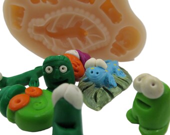 May include: A set of five colorful, hand-painted, cartoon-style figurines. The figurines are made of polymer clay and feature various characters, including a green monster with large eyes, a blue creature with a yellow belly, and a green frog with white eyes.