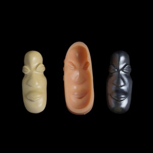 May include: Three face molds, one in beige, one in peach, and one in silver. Each mold is shaped like a human face with closed eyes and a slight smile.
